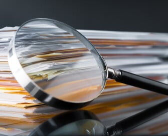 close up of magnifying glass resting on piles of paper