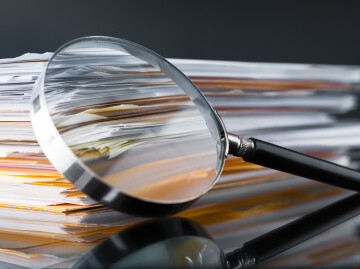 close up of magnifying glass resting on piles of paper