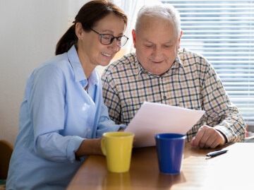 lady helping an older male to read a piece of paper sat at a table